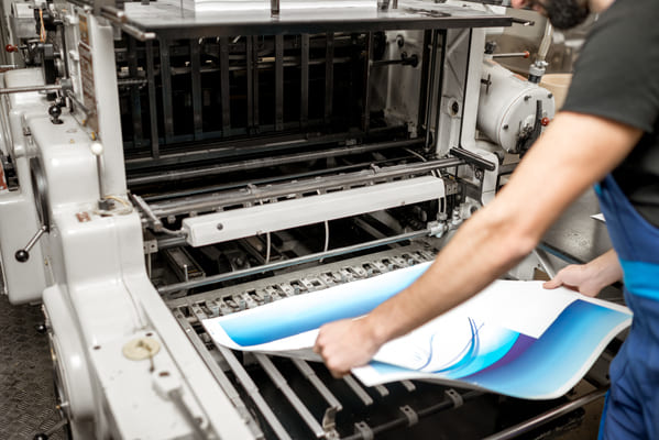 Pracownik wyciąga wydrukowany arkusz papieru z drukarki cyfrowej