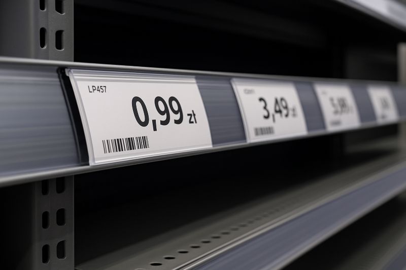Zbliżenie na etykiety cenowe w postaci pasków umieszczone w listwach na półkach sklepowych