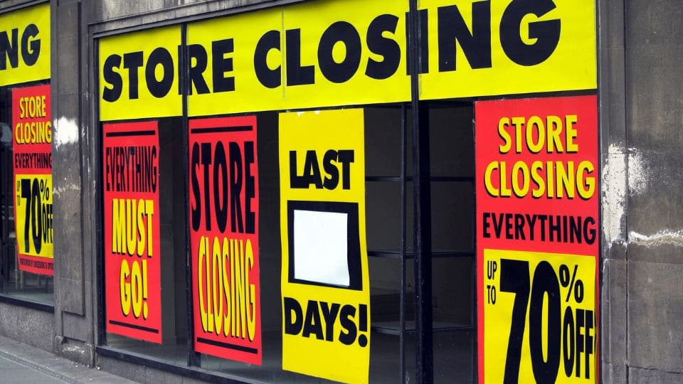 Oklejona witryna przed sklepem w żółte i czerwony naklejki informujące o zamknięciu sklepu